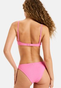 Růžový bikini set s texturovaným vlnitým vzorem. Nastavitelné tenké ramínka a háčkový uzávěr na zadní straně topu. Vysoké kalhotky.