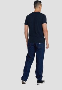 Camiseta de algodón azul marino con mangas cortas y vaqueros de mezclilla oscura. Presenta un ajuste clásico de pierna recta y costuras en contraste. Zapatillas negras.