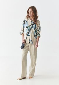 Blomster mønstrede lys beige linned skjorte med optrukne ærmer, kombineret med lys beige linned bukser og minimalistiske flade sandaler; sort crossover taske medfølger.