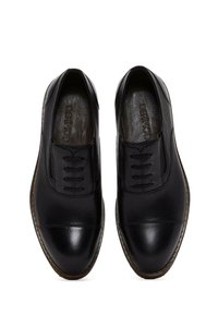 Scarpe in pelle nera con una finitura liscia e strutturata, caratterizzate da un design con allacciatura e una punta arrotondata. Branding discreto sulla soletta interna.