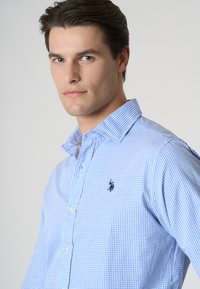 Camicia a quadri azzurri con design button-up, caratterizzata da un colletto classico e un piccolo logo ricamato sul lato sinistro del petto.