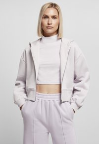 Lys lilla kort t-skjorte med glidelås foran og snor. Kombinert med høy midje lavendel joggebukser med sidelommer.