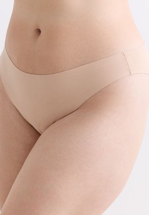 Nahaufnahme des Unterbauchs und der oberen Oberschenkel einer Person, die nahtlose beiger Unterwäsche vor einem einfarbigen Hintergrund trägt.