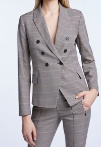 Blazer croisé et pantalon assorti avec un motif à carreaux, dotés de boutons noirs, de revers à pointe et de poches latérales.