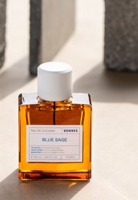 Bärnstensfärgad glasflaska med ett vitt lock, märkt "BLUE SAGE," med en minimalistisk design. Storlek: 50 mL. Strukturerad yta med en tydlig etikett.