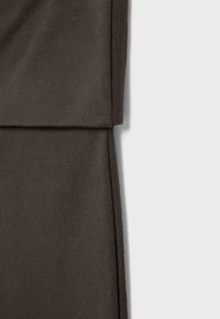 Close-up af mørkebrun stof med synlig søm og detaljer af foldet kant mod en ensartet lys baggrund.