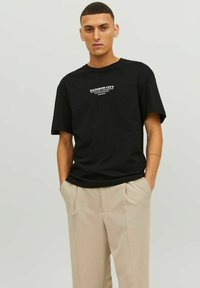 Must mustri t-särk lühikeste varrukatega, millel on valge tekst "RAINBOW CITY". Kanda beežide volditud pükstega. Lihtne disain ja lõdva istuvusega.