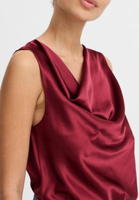 Burgundowa satynowa bluzka z drapowanym dekoltem, bez rękawów, o gładkiej fakturze, eksponująca eleganckie fałdy materiału.