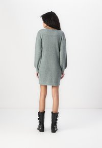 Trikotāžas kleita gaiši zaļā krāsā, līdz vidusceļam, ar gariem bumbierveida piedurknēm un ribota apdare. Apvienota ar melnām augstiem zābakiem līdz ceļiem ar sprādzēm.