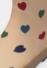 Μπεζ λαστιχένια μπότα με διάσπαρτα κόκκινα, μπλε και πράσινα σχήματα καρδιάς τυπωμένα στην επιφάνεια.