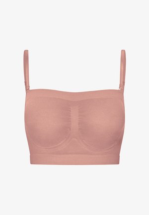 Krøllet hår kvinde med tatoveringer bærer en lilla krydsrem cropped top og højtaljede biker shorts og står mod en hvid baggrund.