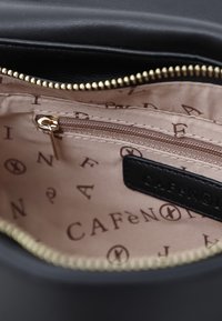 Interno di una borsa a tracolla in pelle nera, con una tasca con zip, foderato in tessuto beige con motivi a logo marroni e una zip dorata.