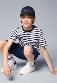 T-shirt à rayures à manches courtes en bleu marine et blanc, short bleu marine, baskets blanches avec accents bleu marine, et casquette de baseball bleu marine avec logo.
