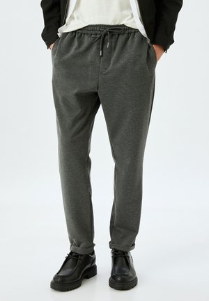 Pantalones de chándal grises fabricados con una tela suave y texturizada. Cuentan con una cinturilla elástica con cordón y bolsillos laterales. Combinados con zapatos negros.