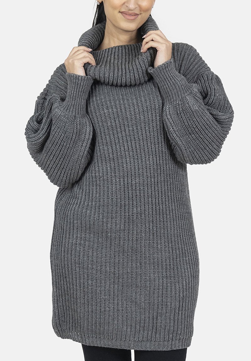 Grijze gebreide trui met een hoge col en volumineuze mouwen. Heeft een geribbelde textuur en een losse pasvorm. Eindigt net boven de heupen.