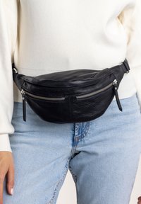 Leather black fanny pack with a curved design, two zippered compartments, and adjustable strap. Textured finish with silver hardware accents.