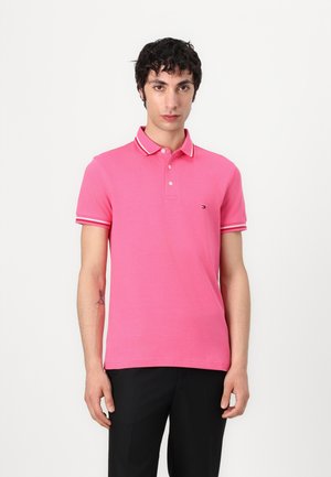 Polo shirt rose à manches courtes avec col blanc et rayures sur les manches. Tissu en coton texturé avec un petit logo sur la poitrine gauche.
