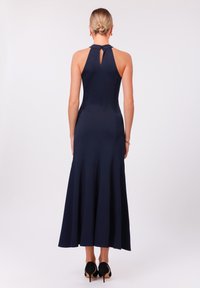 Marine halter-neck jurk met een keyhole rug, aangesloten lijfje en uitlopende rok. Gladde stof, afgewerkt met zwarte hoge hakken.
