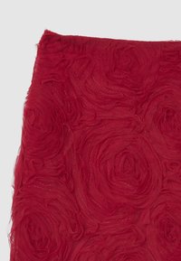 Tessuto rosso con un motivo a rose testurizzato e dettagli a strati e arricciati. Il materiale appare leggero con una leggera lucentezza.