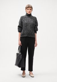Blīvs melnbalts adīts turtlenecks džemperis, melnas svītrainas bikses, beigu zābaki, un melna somiņa.