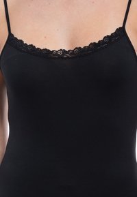 Close-up of a black camisole with thin straps and lace trim worn on a person's upper torso.