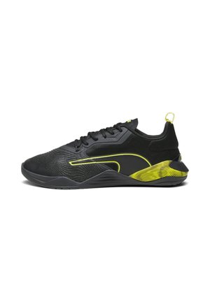 Chaussure de sport noire avec lacets noirs, lignes d'accent jaune néon, semelle texturée et boucle au talon sur fond blanc.