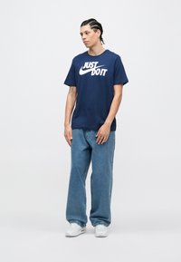 Μπλε βαμβακερό μπλουζάκι με λευκό λογότυπο "JUST DO IT", συνδυασμένο με άνετο μπλε τζιν παντελόνι και λευκά αθλη�τικά παπούτσια. Λείο ύφασμα.