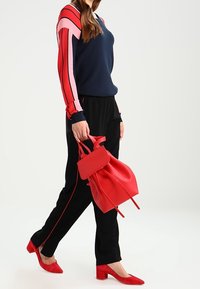 Czerwono-różowy sweter z długim rękawem w paski, czarne spodnie z czerwonymi lamówkami, czerwona torebka oraz pasujące buty na słupku.