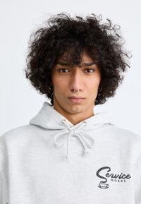 Gray hoodie with drawstring and ribbed cuffs, featuring a logo print on the left chest. The fabric appears soft with a slight texture.