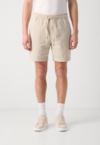 Shorts beiges en tissu texturé, avec une taille élastique et un cordon de serrage, ainsi que des poches latérales. Assortis à des sneakers claires et des chaussettes blanches.