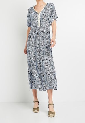 Femme portant une robe midi bleue et blanche à motif cachemire avec manches courtes et des sandales compensées espadrilles beige.