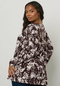 Braun- und cremefarbener Langarmoberteil aus strukturiertem Stoff mit gepunktetem Muster, lässiger Passform und rundem Halsausschnitt.