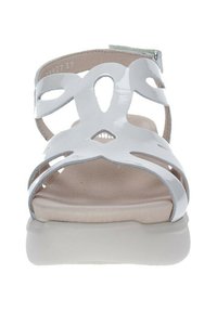 Sandalias blancas de material brillante, con diseños recortados, una plantilla acolchada beige y una suela baja y texturizada.