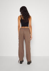 Lichte brown cargobroek met zijzakken, losse pasvorm, elastische tailleband en aantrekkoorden. Gepaarde met een zwart mouwloos topje.