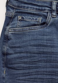Dark blue denim jeans with a smooth texture, five-pocket design, and contrasting yellow stitching. Features a small, branded metal button.
