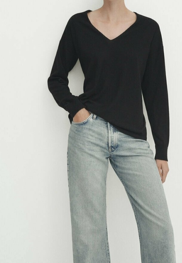 Zwarte lange mouwen V-hals top gedragen met lichtblauwe wijde jeans. De top heeft een ontspannen fit; de jeans hebben een klassieke denimtextuur.