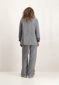 Grijze wollen mix pak met een op maat gemaakte blazer en wijde broekspijpen. Opvallende details zijn de manchetten en de gladde textuur.
