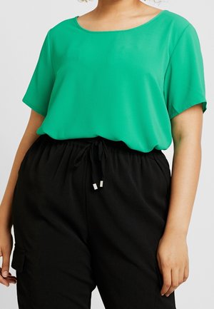 Green short-sleeved top in lightweight fabric with a rounded neckline, paired with black drawstring pants featuring a side pocket.