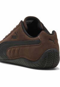 Bruine suède sportschoen met zwarte rubberen zool, voorzien van een gestructureerd ontwerp en logo-accenten. Ronde hiel en gevoerde kraag.