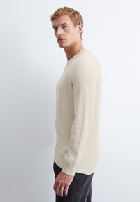 Beige ribbad svett med långa ärmar och rundad halsringning. Mjuk textur och åtsittande design. Bärs med mörkfärgade byxor.