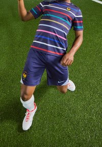 Marinblå randig tröja med röda, blå och rosa horisontella ränder; marinblå shorts; vita strumpor; röd och vit fotbollsskor; med ett höns emblem.