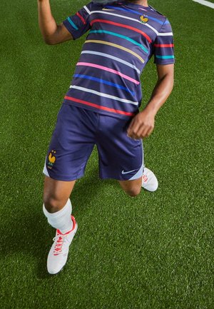 T-shirt rayé bleu marine avec des lignes horizontales rouges, bleues et roses ; shorts bleu marine ; chaussettes blanches ; chaussures rouges et blanches ; arborant un emblème de coq.