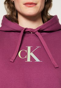 Purple hoodie with a drawstring, featuring a pale green "ck" logo on the chest. Soft fabric and casual design.