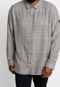 Camisa de manga larga con botones en patrón de pata de gallo negro y blanco con acentos naranjas, que presenta un cuello estándar y un corte relajado.