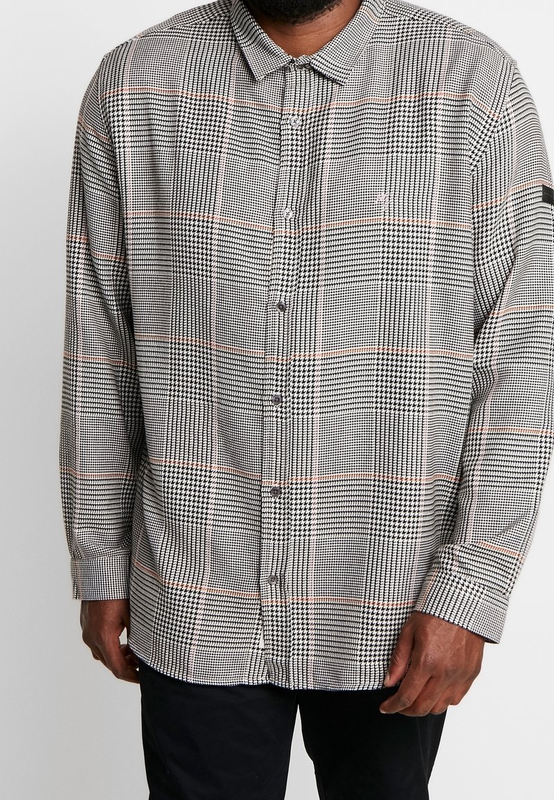 Camisa de manga larga con botones en patrón de pata de gallo negro y blanco con acentos naranjas, que presenta un cuello estándar y un corte relajado.