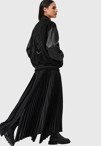 Giubbotto bomber nero con maniche in pelle, abbinato a una gonna a pieghe nera e stivaletti. Materiali texturizzati creano un look stratificato.