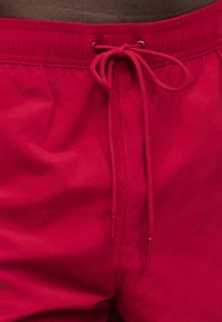 Κόκκινα μαγιό βερμούδα με ελαστική μέση και δεμένο κορδόνι στο κέντρο μπροστά.