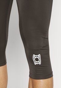 Fekete sportleggings sima textúrával, térdhez érő hosszban, alsó lábrészén fehér logóval. Varrás nélküli dizájn a kényelemért.