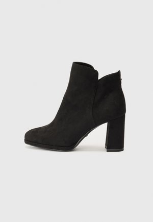 Mustmust musta pahklajaab, ümarate ninade ja lõikega detailiga kaelas ning paksu kõrge kontsaga. Sile tekstuur, nähtavad riistvara pole.