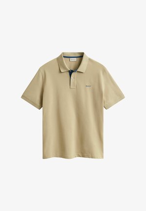 Beigenvärinen lyhythihainen poolopaita, jossa on kaksinappinen nappilista, pieni sininen logo vasemmassa rinnassa ja kontrastivärinen kauluksen sisävuori.